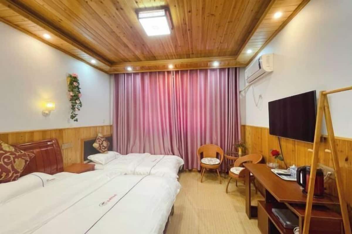 A hotel room with wooden ceiling, a bed, a desk, a chair, a TV, and a curtain.