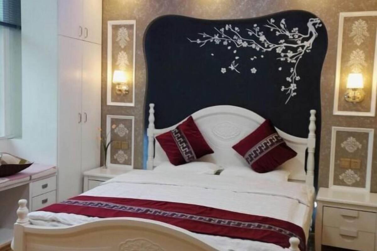 A bedroom with a bed, nightstands, wall sconces, and a wardrobe.
