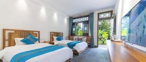 Quarto de hotel com duas camas, uma escrivaninha e uma janela grande com vista para o verde.