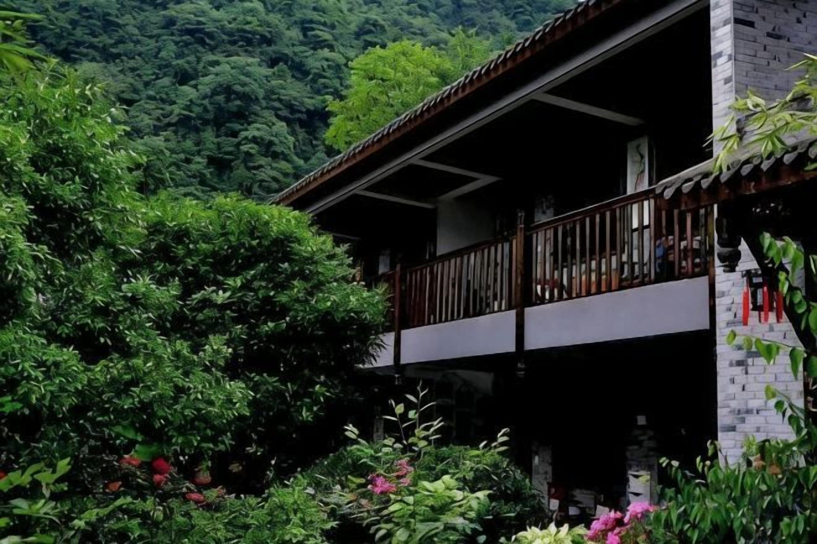 A two-story building with a balcony, surrounded by lush greenery.