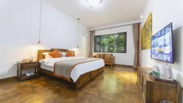A bedroom with a large bed, bedside tables, a wooden dresser, a TV, and a window with curtains.