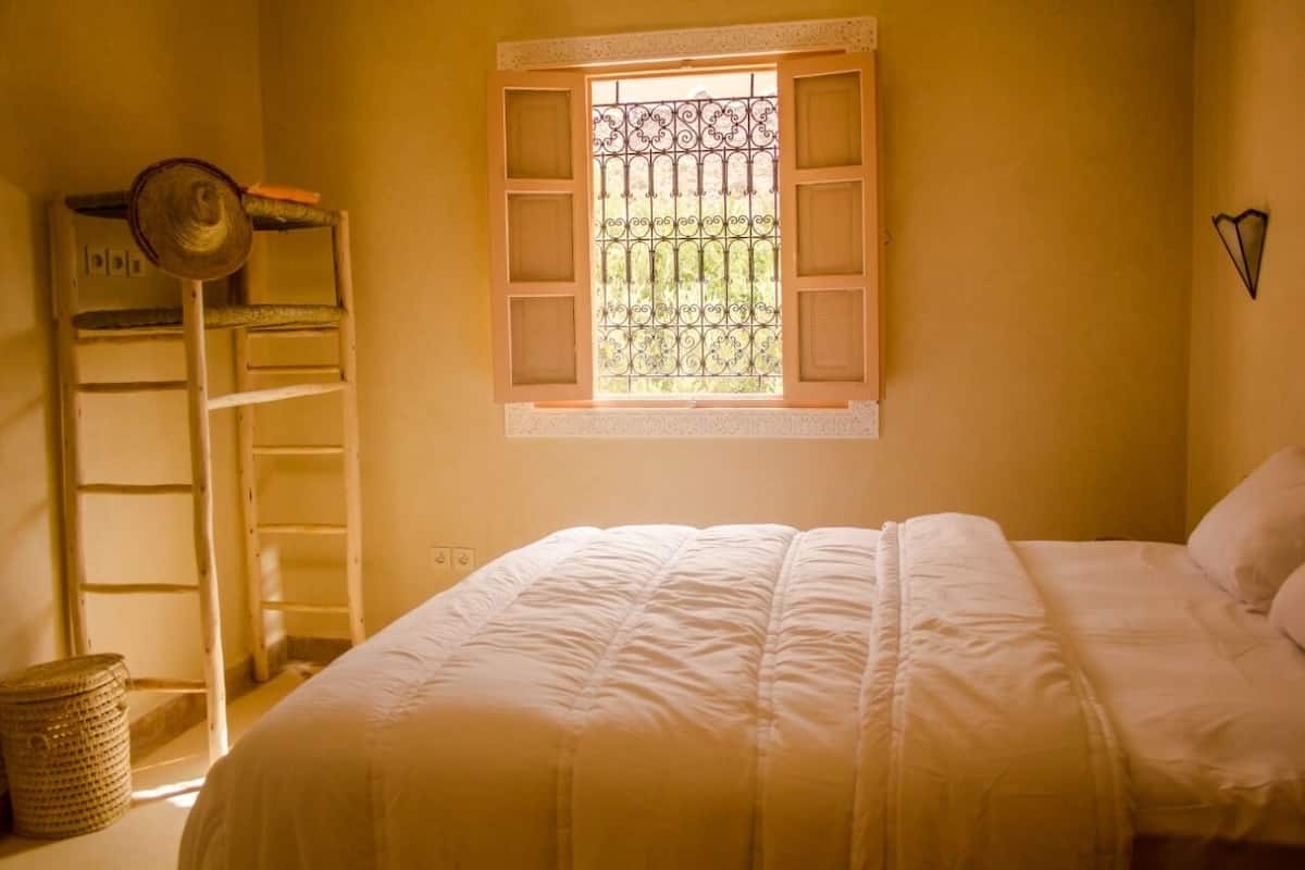 A bedroom with a bed, a window with a metal grill, a ladder, and a basket.