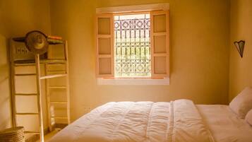 A bedroom with a bed, a window with a metal grill, a ladder, and a basket.