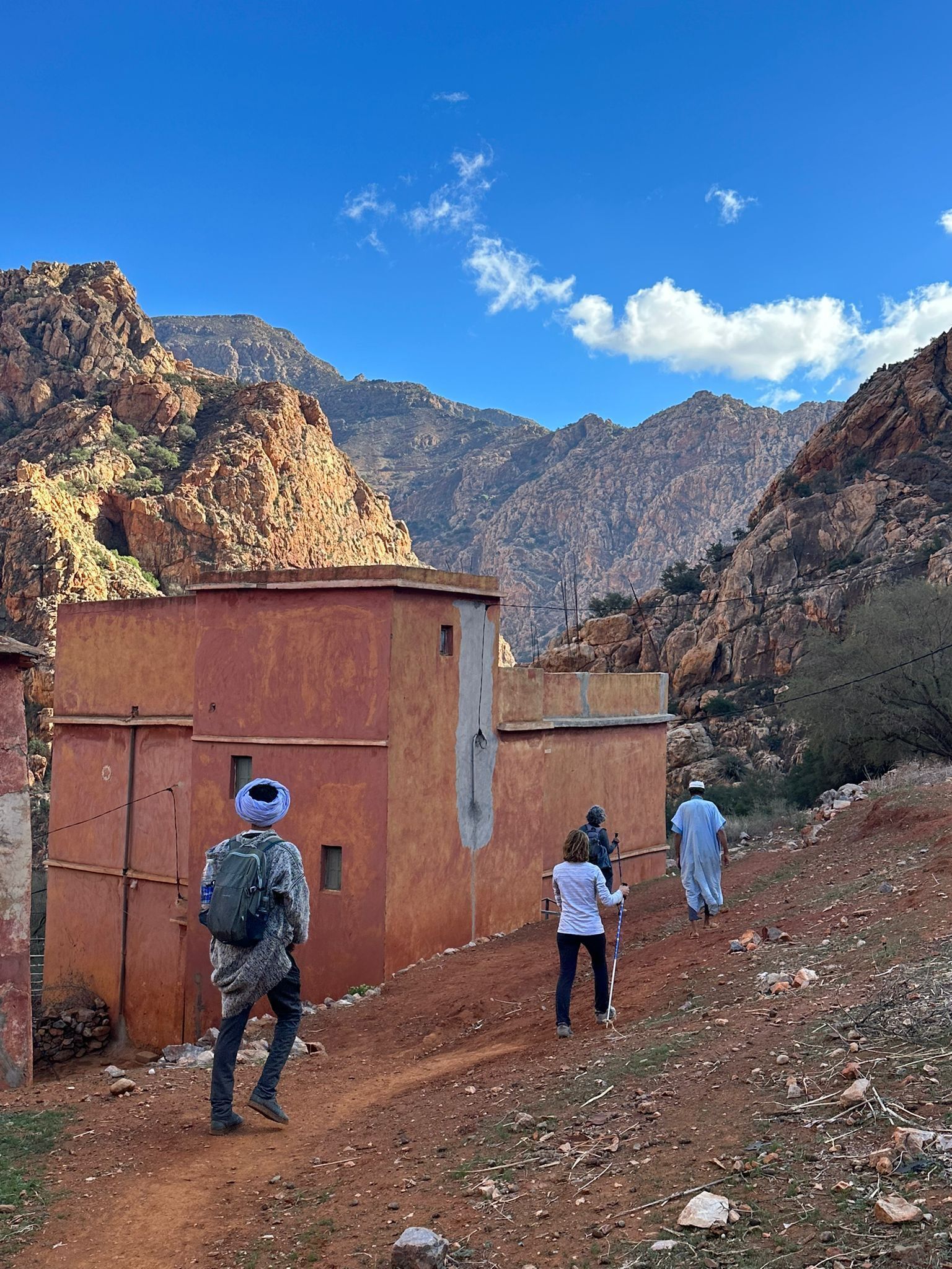 Paesaggio montuoso e impervio con un sentiero sterrato che conduce a un piccolo edificio rustico dotato di tetto piatto.