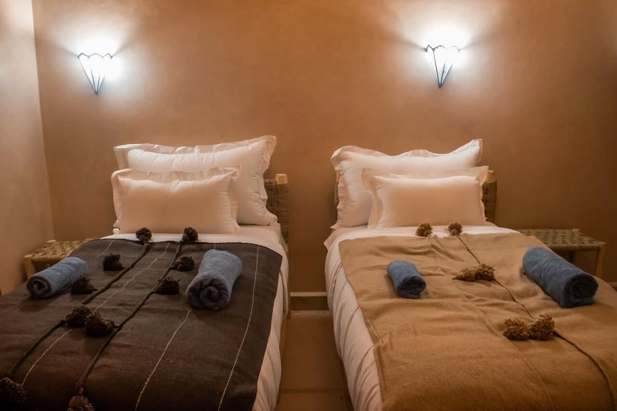 Two single beds with white pillows and brown blankets, each with rolled towels and decorative pine cones.