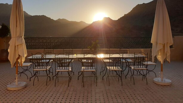 A terrace with tables and chairs facing a mountain view at sunset. - Dar Ajgal (Tanalt)