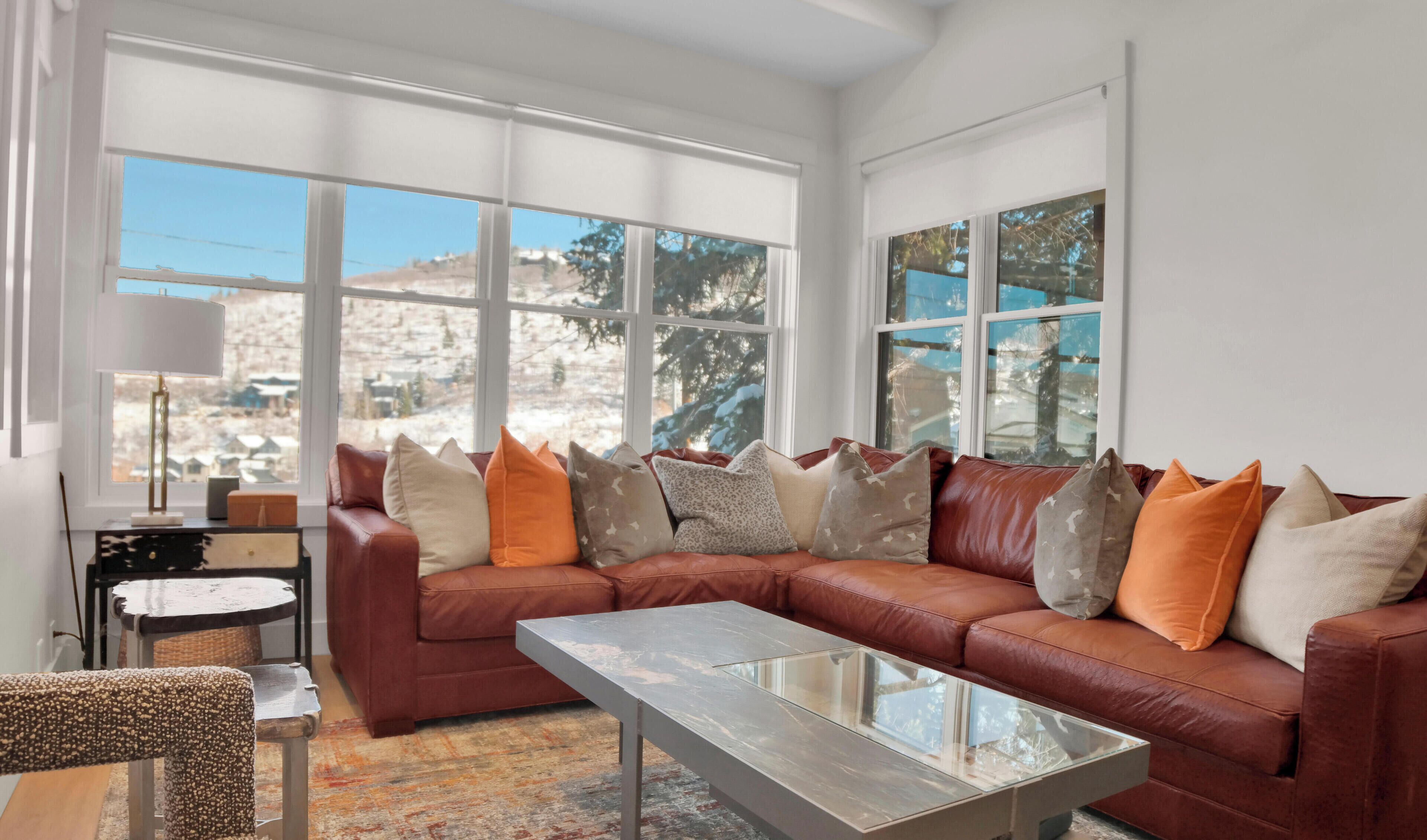 Ein modernes Wohnzimmer mit Ledersofa, Glastisch und großen Fenstern mit Blick auf eine verschneite Landschaft.