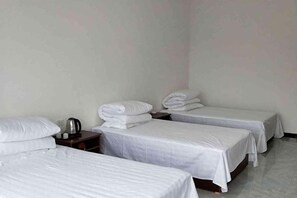 A hotel room with three single beds, a nightstand with a kettle, and plain walls. - Guo's Farmhouse (Pianguan)