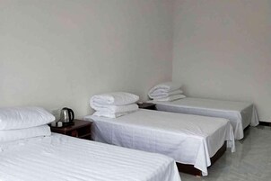 Habitación de hotel con tres camas individuales, una mesita de noche con hervidor y paredes lisas.