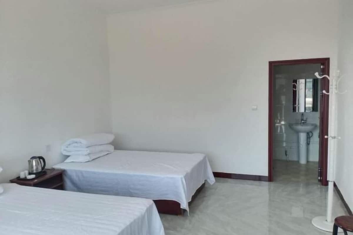 A hotel room with two beds, a nightstand with a kettle, a mirror, and a bathroom visible through an open door.