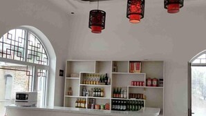 Una zona de bar con estantes llenos de diferentes bebidas, un mostrador blanco y faroles rojos colgantes.
