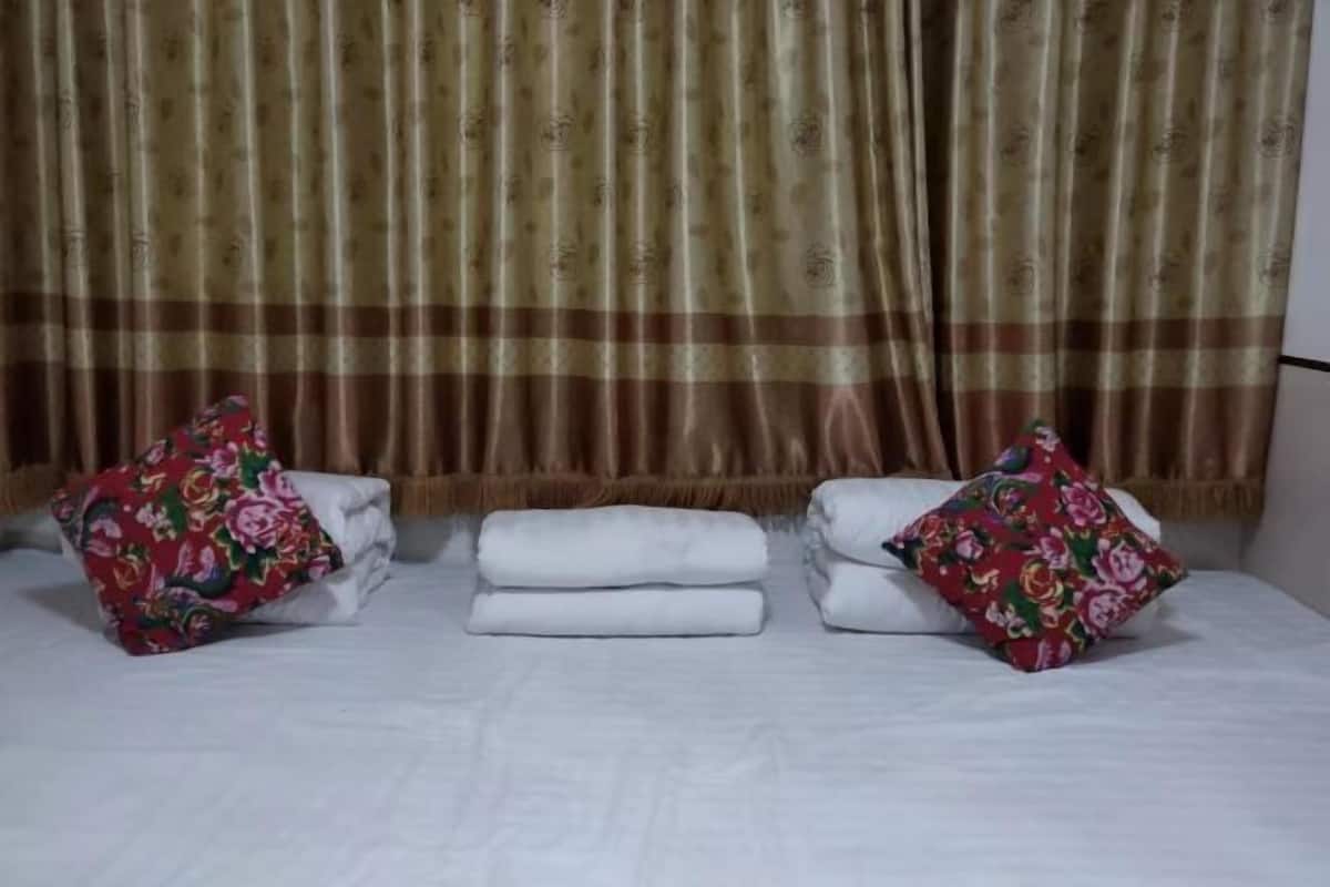 A bed with white linens, two floral pillows, and a curtain with a pattern.
