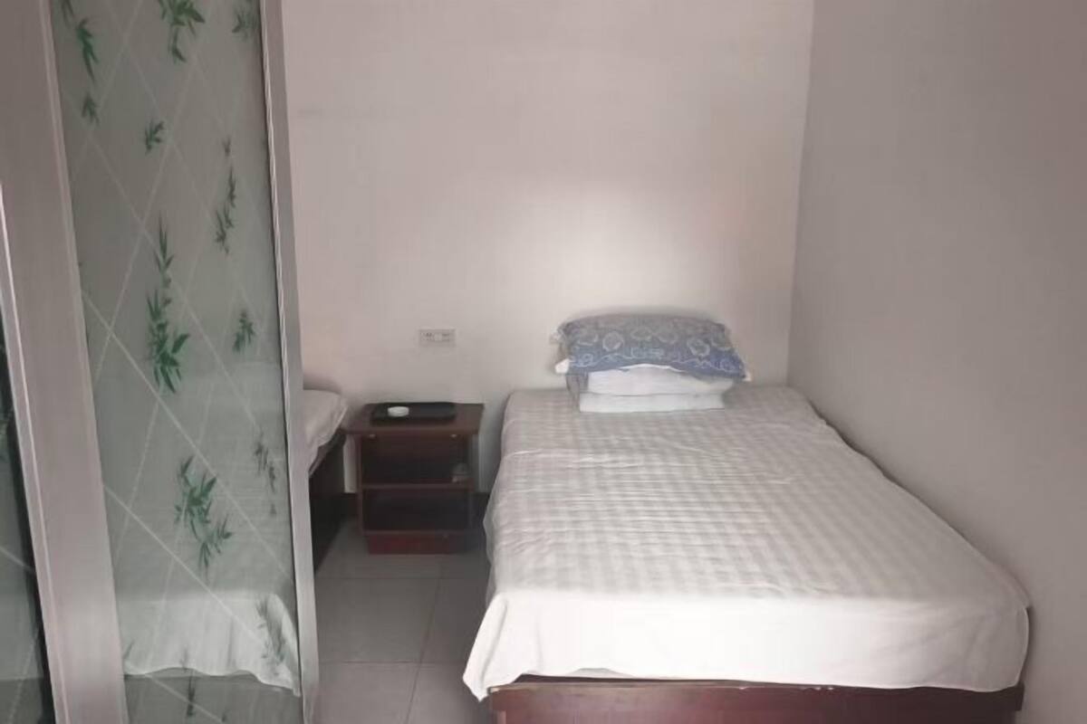 A small, single-bed room with a wooden headboard, a bedside table, and a patterned curtain.