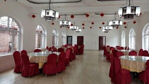 Un amplio salón con mesas redondas y sillas rojas, ventanas arqueadas y faroles colgantes.