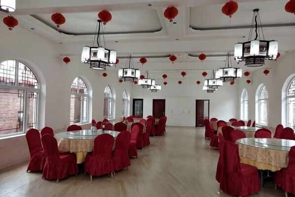 A large hall with round tables and red chairs, arched windows, and hanging lanterns. - Guo's Farmhouse (Pianguan)