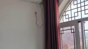 Una habitación con un ventanal grande, una cortina y un enchufe en la pared.
