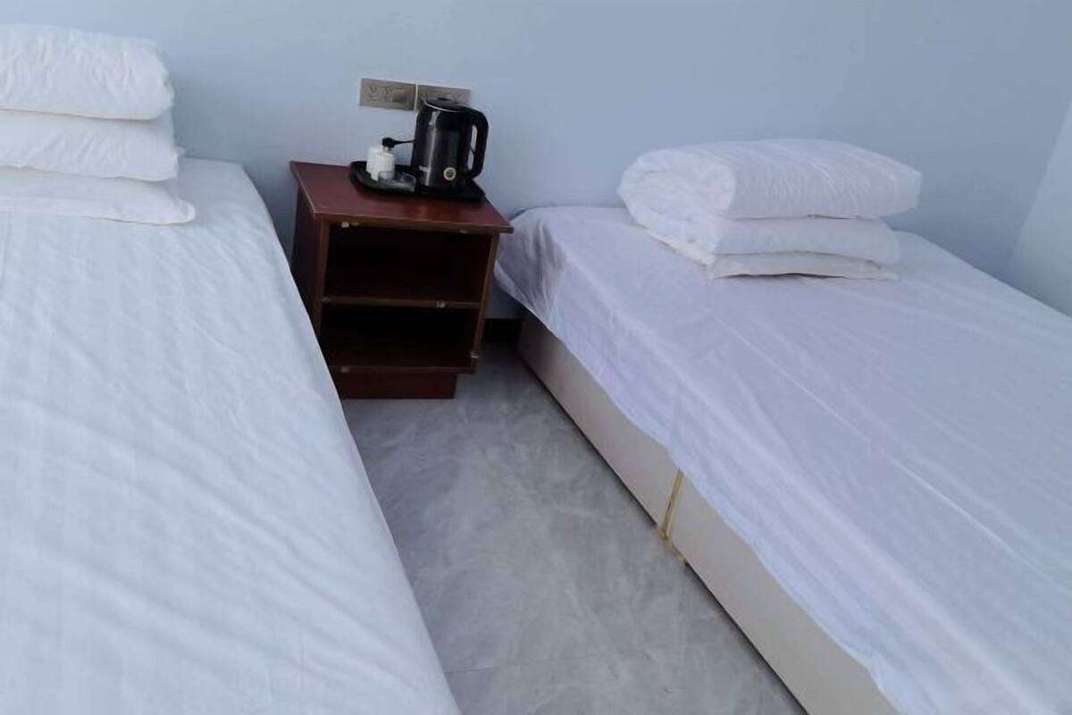 A small, clean room with two single beds, a nightstand with a kettle, and a wall socket.