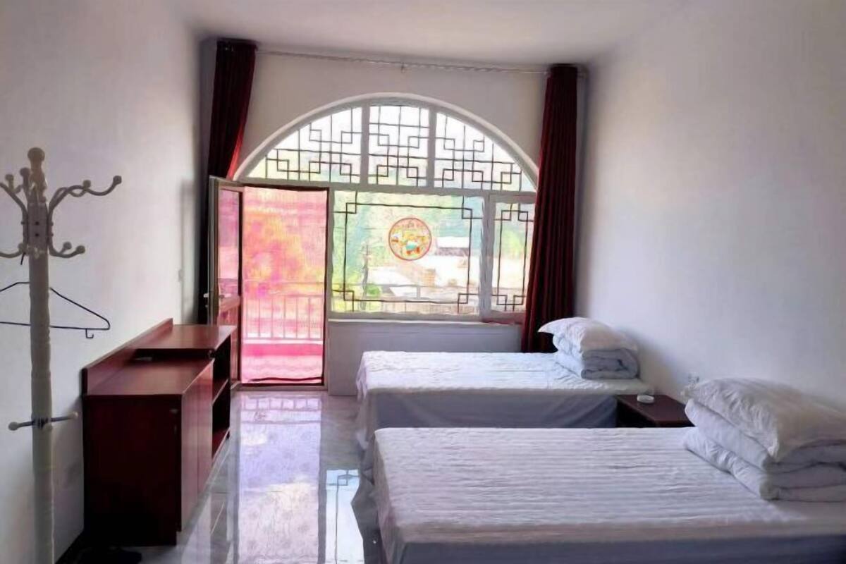 A hotel room with two beds, a coat rack, and a window with a view of the outside.