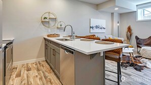 A modern kitchen with a central island, stainless steel appliances, and a minimalist design. - Blatchford - 2 Queen Beds - W/D to NAIT (Northwest)