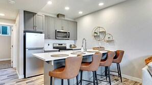 A modern kitchen with grey cabinets, a built-in microwave, and a central island with bar stools. - Blatchford - 2 Queen Beds - W/D to NAIT (Northwest)