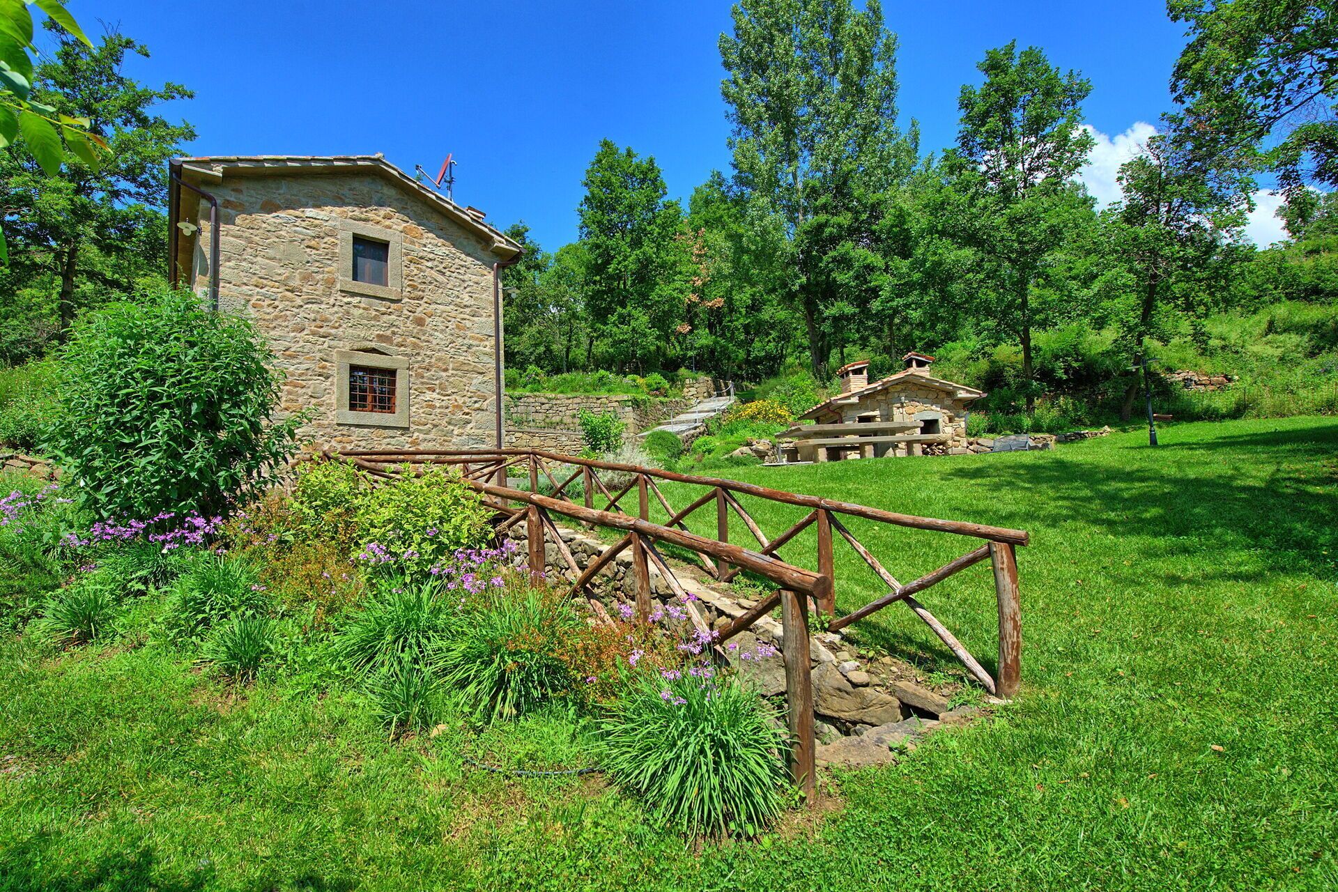A stone building with a wooden bridge, surrounded by lush greenery and trees.