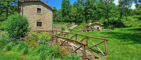 A stone building with a wooden bridge, surrounded by lush greenery and trees.