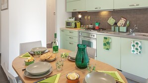 A modern kitchen with green cabinets, a microwave, stove, and various kitchen utensils. There is a dining table set with plates, bowls, and glasses.