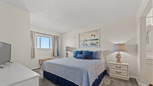 Un dormitorio con cama, mesitas de noche, lámpara, un cuadro y ventana con cortinas.