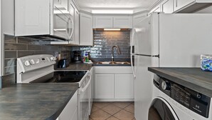 Una cocina compacta con muebles blancos, horno integrado, lavavajillas y lavadora.