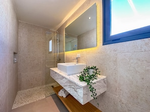 A modern bathroom with a glass-enclosed shower, a white sink, and a mirror with a yellow light strip. - Elegant and spacious Penthouse with Ocean View (Punta Cana)