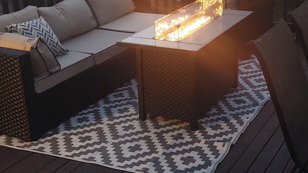 An outdoor deck with a sofa, a table with a fire feature, and a patterned rug.