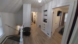 A hallway with a staircase leading to a second floor, a small table with chairs, and a closet with shelves.