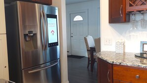 A stainless steel refrigerator with a digital interface, a dining area with a wooden table and chairs, and a kitchen counter with a marble top.