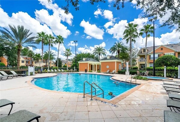 A swimming pool with lounge chairs and palm trees, surrounded by buildings.