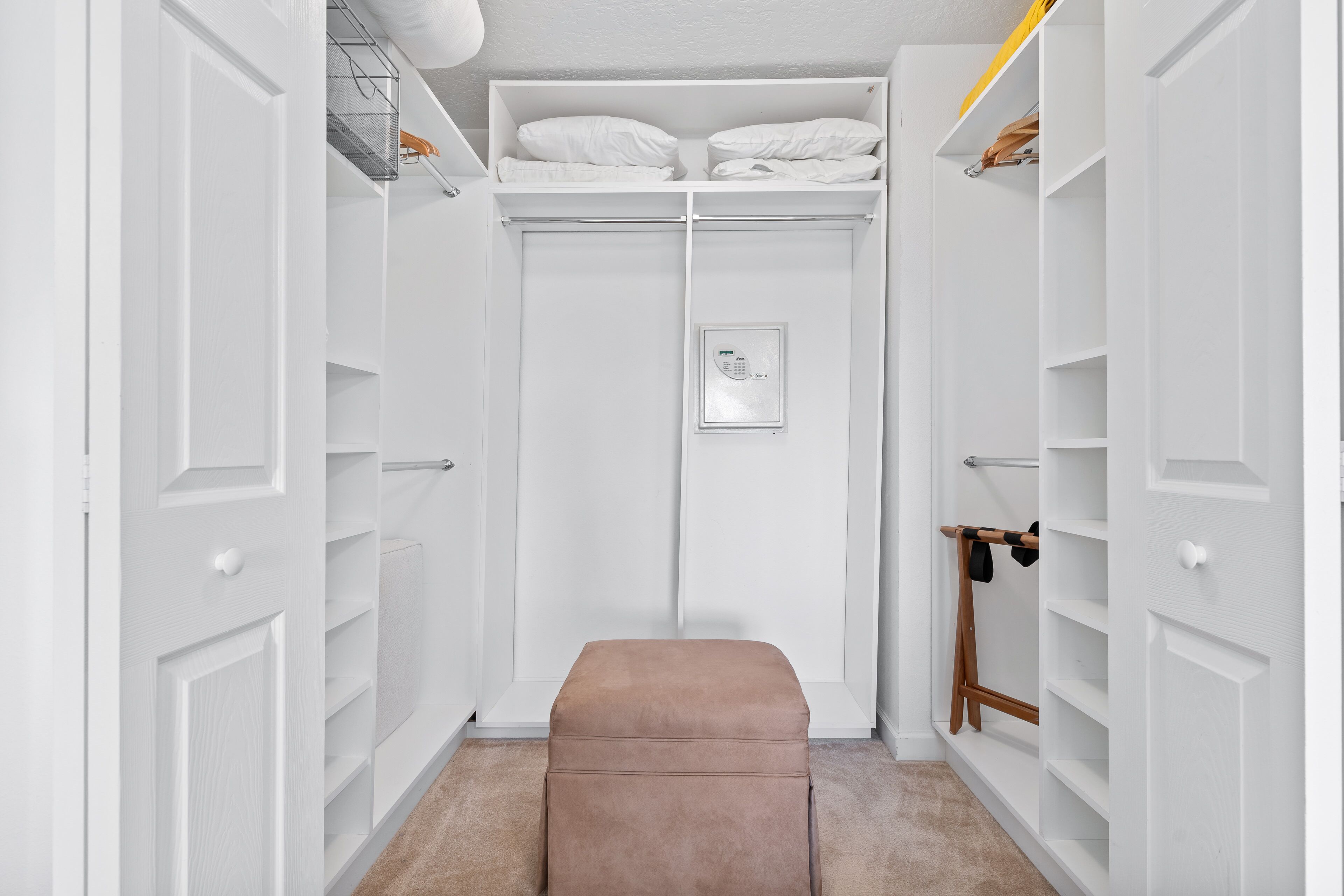 A walk-in closet with white doors, shelves, and a bench.