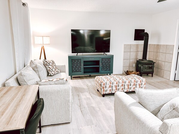 A living room with a sofa, ottoman, TV, cabinet, and a wood-burning stove.