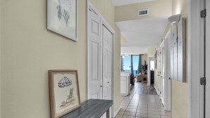 A hallway with a tiled floor, white doors, and framed artwork on the walls. - ⭐Beachfront-Gulf Views-Pools and Hot Tubs-3BR Summerwind 1301⭐ (Navarre)