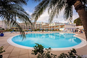 A swimming pool surrounded by palm trees and a hotel building with multiple balconies.