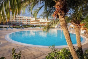 Un'area piscina con una vasca circolare, palme e un edificio sullo sfondo con numerosi balconi.