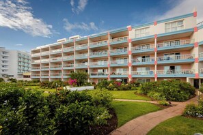 A multi-story hotel with balconies, a garden area, and a clear sky.