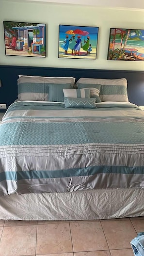A bed with a quilted cover, a headboard, and a wall with three paintings. - Grand Getaway - Royal Retreats at Maho Beach Studio (Lowlands)
