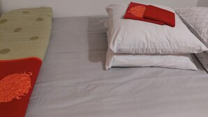 A single bed with a white mattress, a green polka-dotted pillow, and a red floral pillow. - Studio in the heart of Montmartre (Paris)