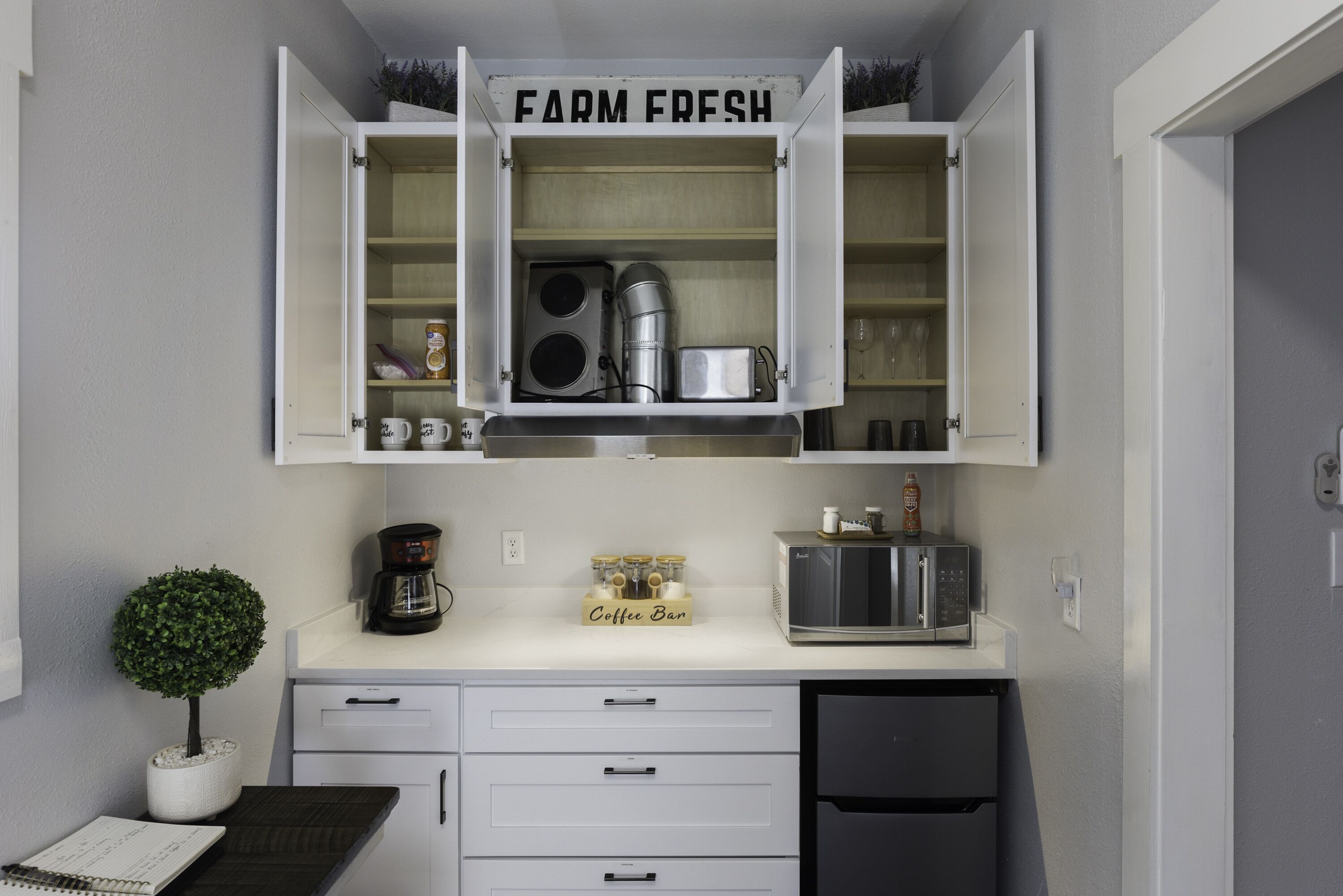 A compact kitchen with a coffee station, a microwave, and a refrigerator.