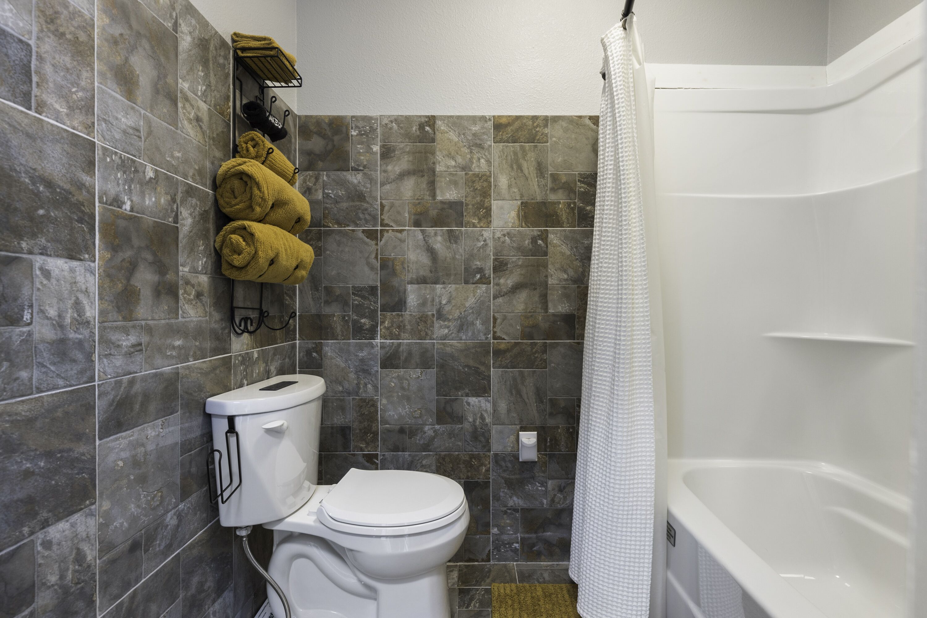 A bathroom with a toilet, a shower with a white curtain, and towels hanging on a rack.