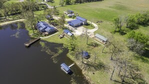 An aerial view of a lakeside property with multiple buildings, a dock, and a boat. - SweetDove Stays-  Suite; w/ Stocked Lake, Secure Parking (Rains County)