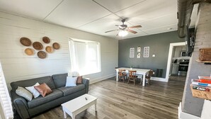 A living room with a gray sofa, white coffee table, and a dining area with a white table and wooden chairs. - Fenced Yard - <1 mile from Purina - No Cleaning Fee (Gray)
