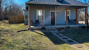 A single-story house with a covered porch, a fenced yard, and a clear blue sky. - Fenced Yard - <1 mile from Purina - No Cleaning Fee (Gray)