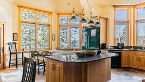 Una cocina con una isla grande, armarios de madera y vistas a árboles a través de amplias ventanas.