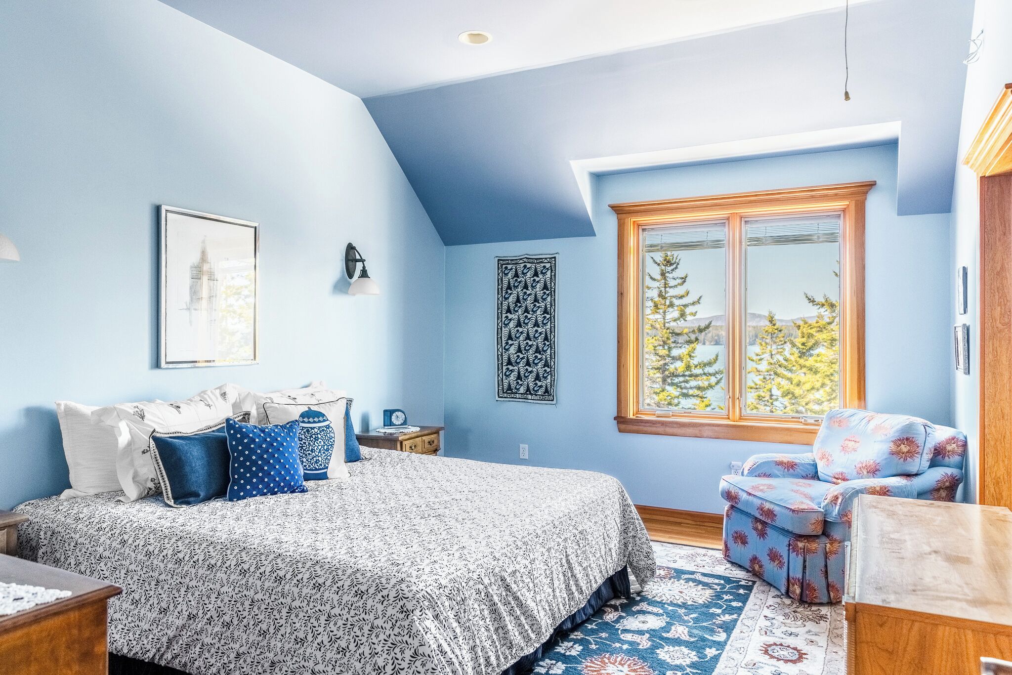 A bedroom with a large bed, a chair, a window with a view, and a patterned rug.