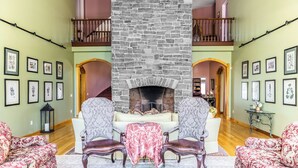 Amplia sala de estar con chimenea de piedra, dos sillones, un sofá y una mesa de comedor.